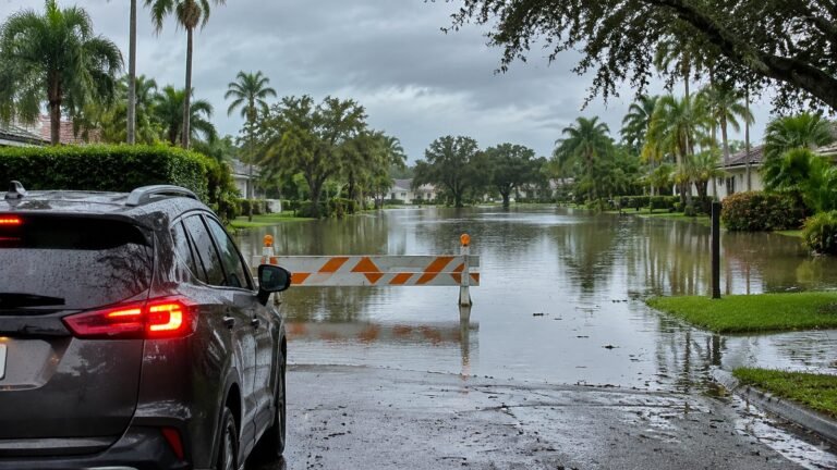Flooded Florida neighborhood street with an orange and white barricade in the water and an SUV stopped at the edge, illustrating flood safety and why you never drive through floodwater